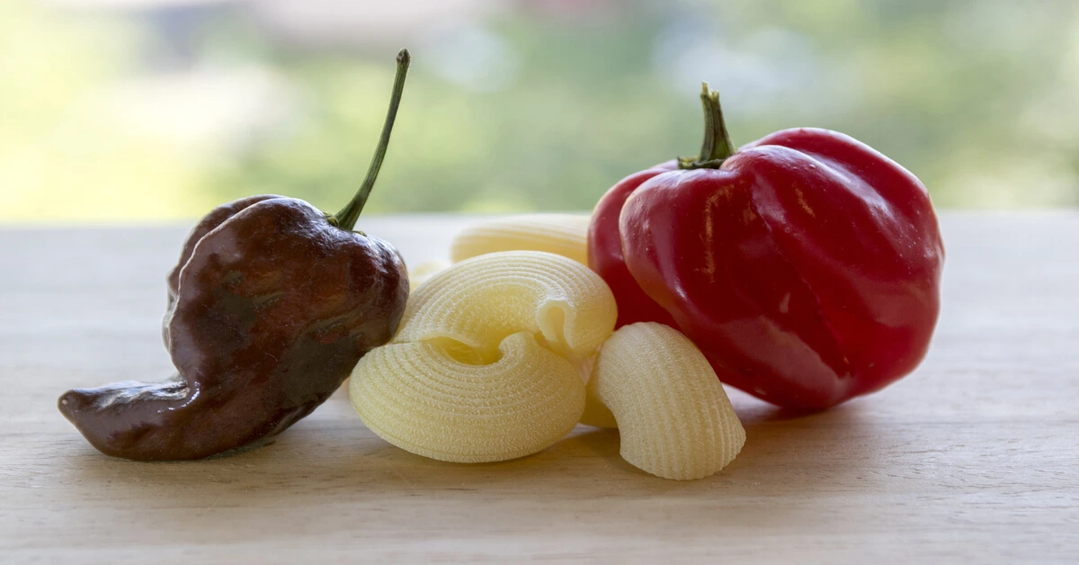 Two peppers sitting on a wood table, chocolate habanero vs habanero.