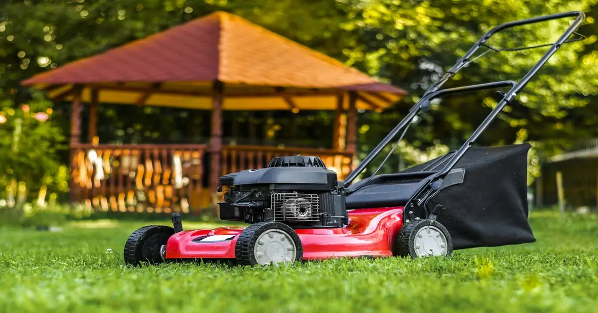 Red and black push lawn mower sitting in yard.