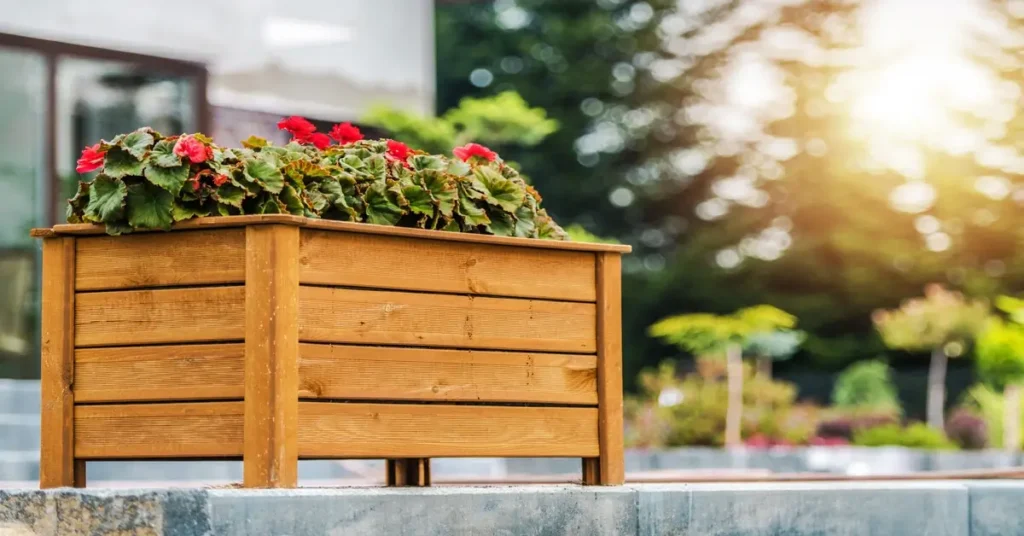 How Long Do Planter Boxes Last? Wooden planter box on deck with red flowers growing.