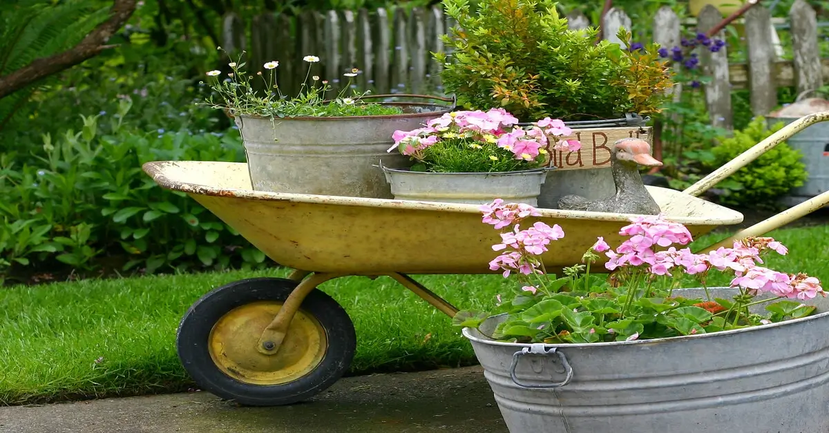 Old yellow wheel barrow with plants in containers as a sustainable gardening technique.