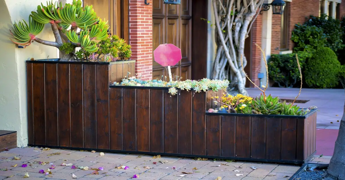 Three tier wooden planter box next to garage doors with various plants growing.